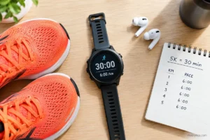 Flat lay of running gear with a GPS watch showing a 6:00 per km pace and a notepad displaying a 30 minute 5K goal, illustrating the pace needed to run a 5K in 30 minutes.